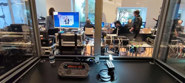 An interpreter’s console on the desk of a booth, looking onto the technical room through the glass.